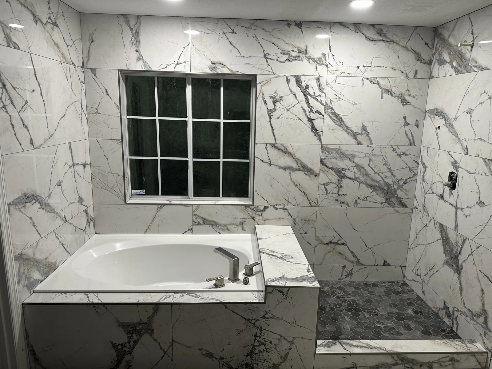 Sanford bath near completion with walls tiled and tub deck wrapped in marble-look porcelain